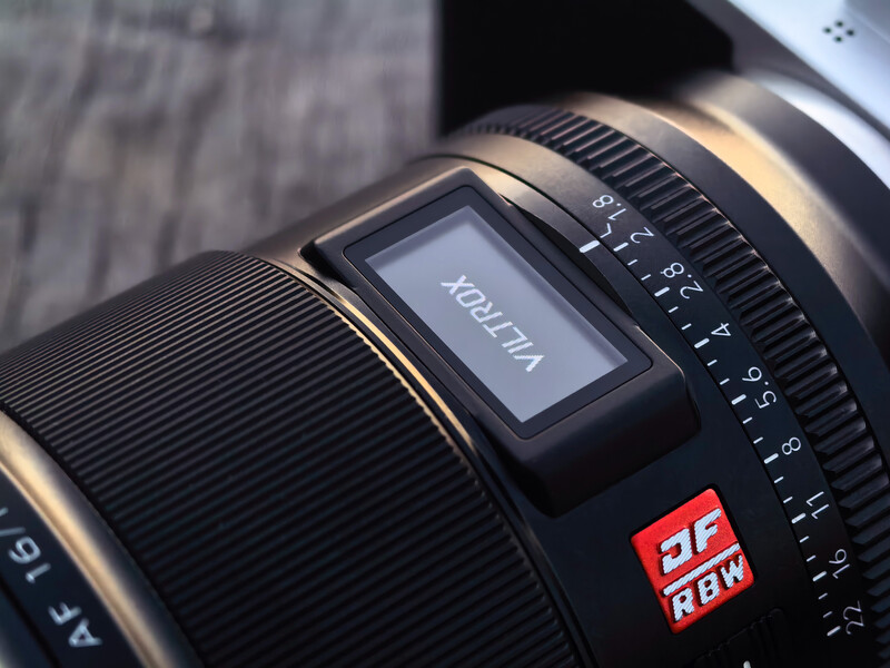 Close-up of a telephoto lens barrel showing focus ring, aperture scale, and red branded badge.