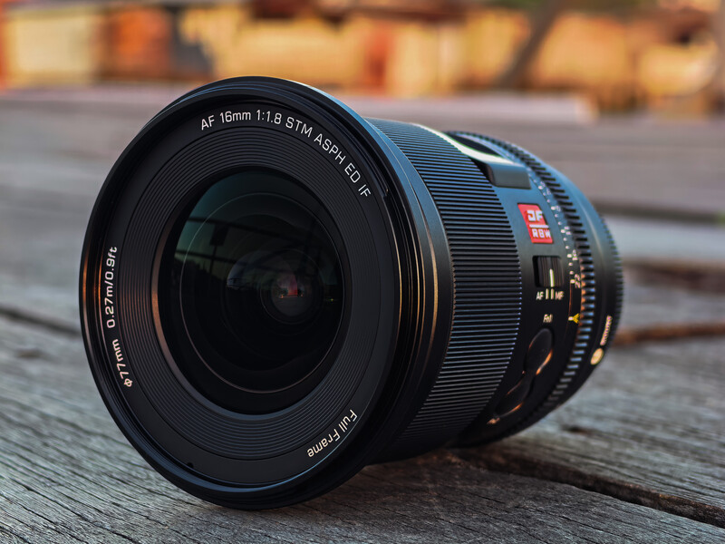 Canon AF 16mm f/1.8 fisheye lens positioned on wooden surface with blurred urban background.