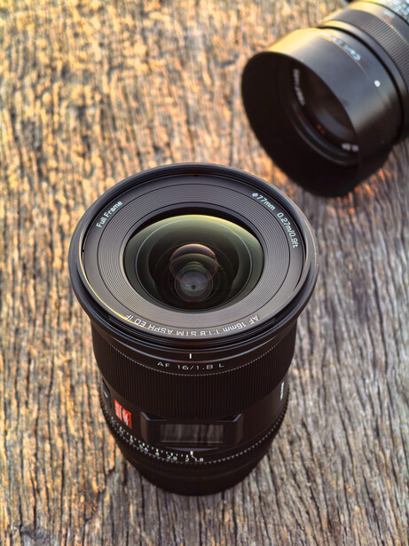 Two camera lenses arranged on a textured wooden surface, with one in sharp focus in the foreground.