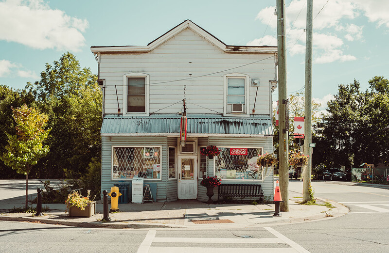 White two-story corner building with turquoise metal railings and storefront windows on ground level.