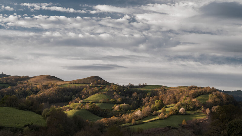 Rolling hills with autumn foliage under dramatic cloudy sky.