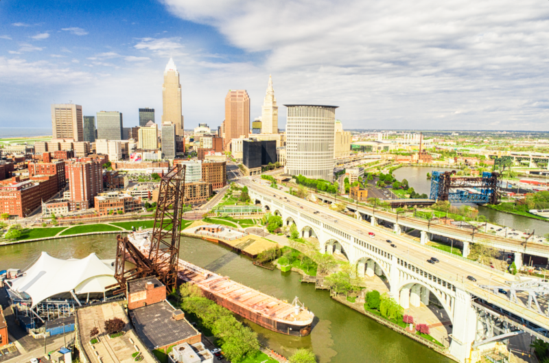 Aerial view of an industrial waterfront district with city skyline and river in the background.