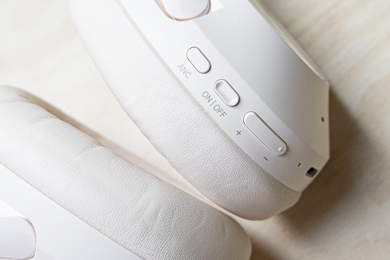White wireless headphones with control buttons displayed on neutral background.