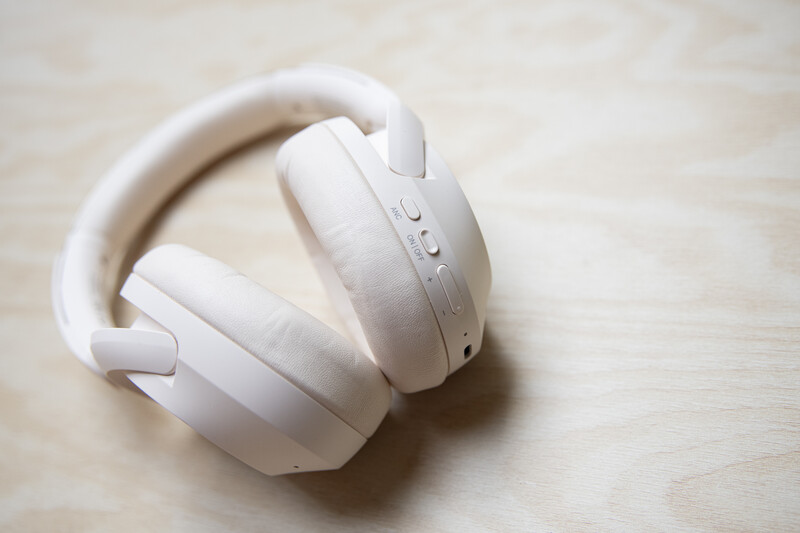 Pair of white wireless over-ear headphones resting on a light wooden surface.