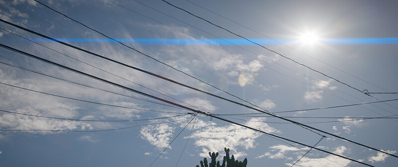 Power lines and utility cables converging against a bright sky with scattered clouds.
