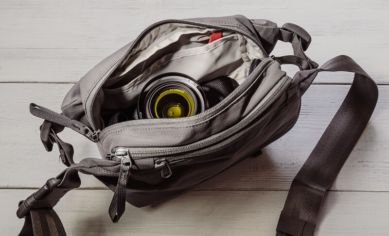 Camera lens with yellow filter stored in open gray padded shoulder bag on white wooden surface.