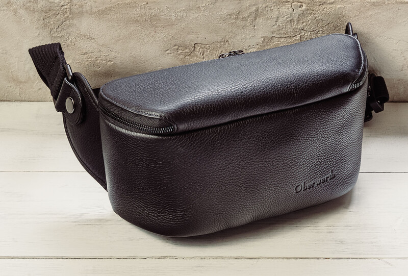 Black leather shoulder bag with textured pebbled surface and adjustable strap on white wooden surface.