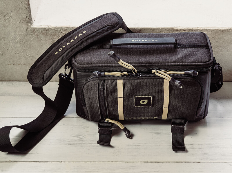 Black and tan camera bag with shoulder strap and multiple compartments displayed on white wooden surface.