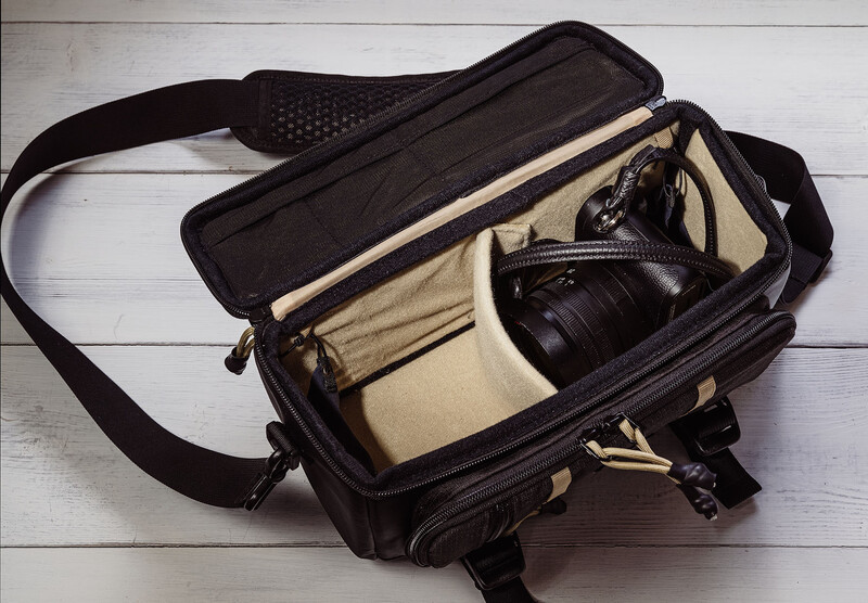 Black camera bag with tan canvas interior holding a mirrorless camera body and lens.