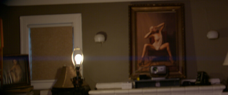 Interior shelf with desk lamp, framed artwork, and decorative items illuminated by warm lighting.