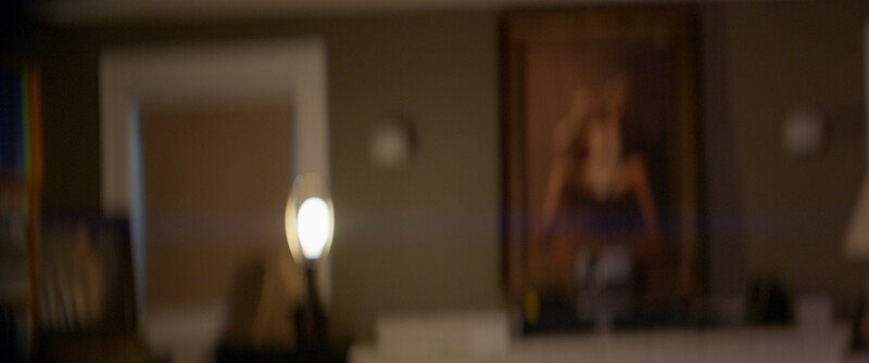 Out-of-focus interior hallway with warm tungsten lighting and framed artwork on walls.