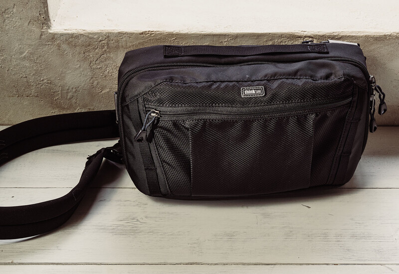 Black nylon camera bag with shoulder strap and multiple zippered pockets on white wooden surface.