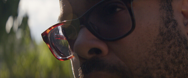 Close-up of a person wearing tortoiseshell-framed sunglasses with a water droplet on the lens.