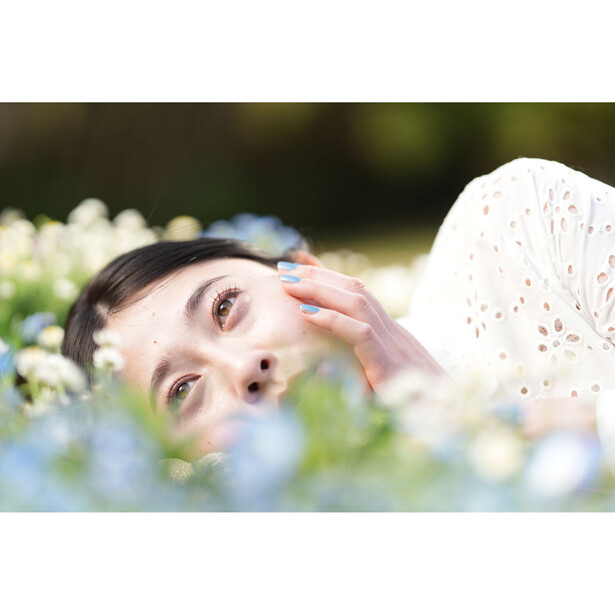 Woman with hand to face among blurred flowers in natural outdoor light.