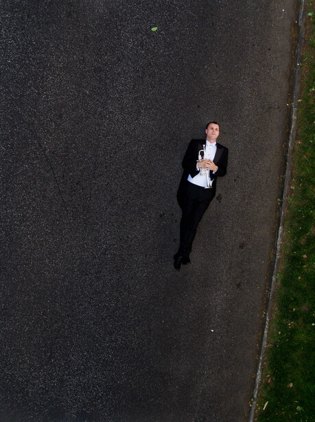 Overhead aerial view of a man in a dark suit jogging on asphalt pavement.