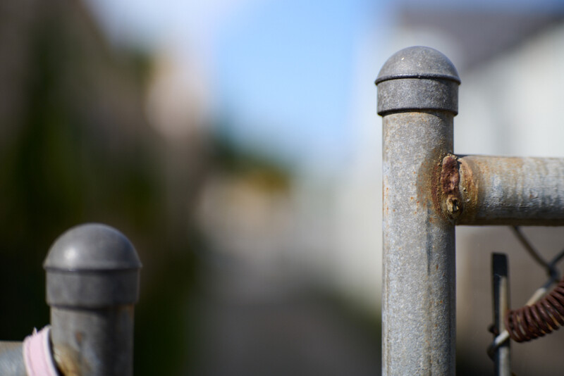 Close-up of weathered metal fence posts with rounded caps, selective focus with blurred residential background.