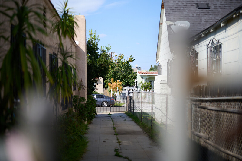 Narrow residential alley between white and tan buildings with soft focus foreground and background.