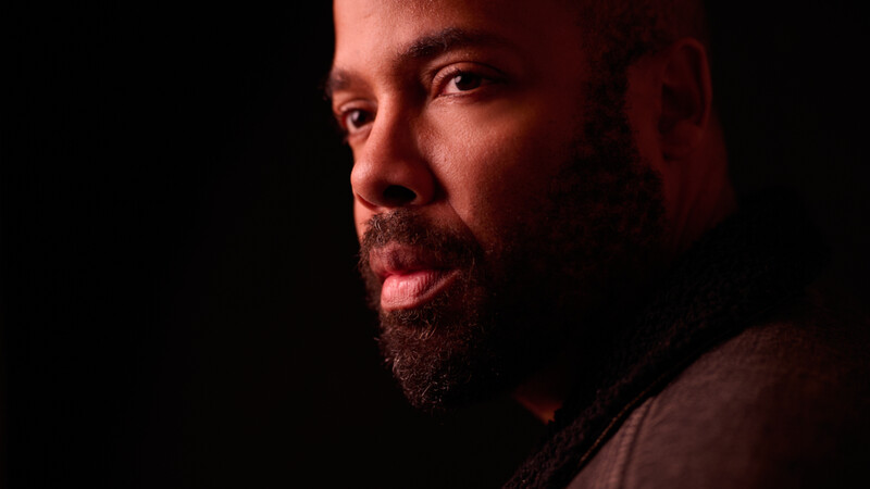 Man with beard in profile against dark background, lit by warm side lighting.