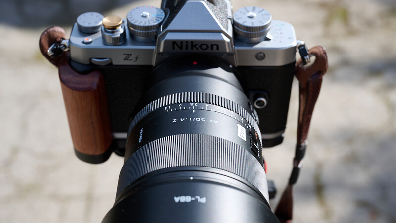 Nikon Z f camera with wooden grip straps and telephoto lens mounted, shot from above on outdoor surface.