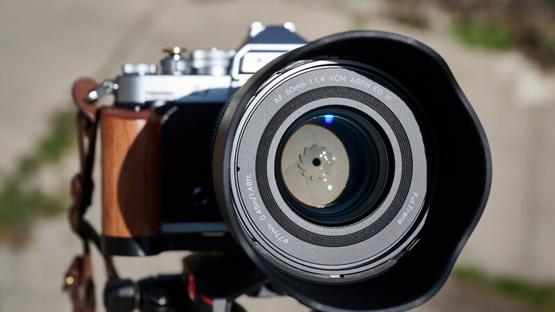 Vintage rangefinder camera with lens hood and brown leather strap, shot from front angle in daylight.