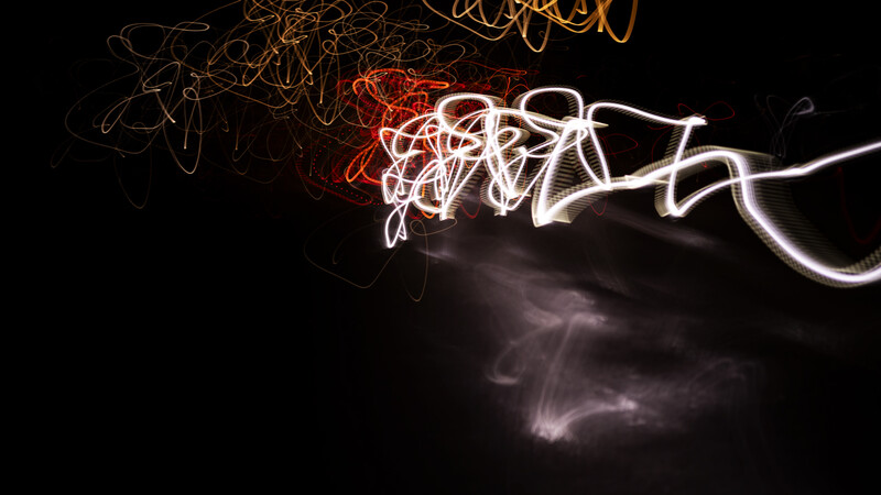 Light painting photograph with tangled white and red neon lines against dark background.