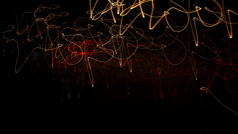 Long-exposure light painting with golden and red streaks against a black background.