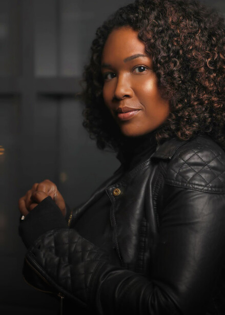 Woman in black leather jacket against dark background, looking directly at camera.