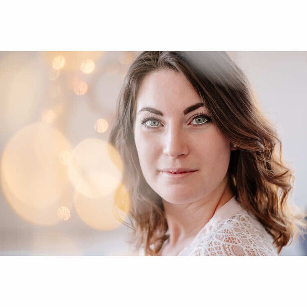 Woman with long brown hair and blue eyes looking at camera with soft smile.
