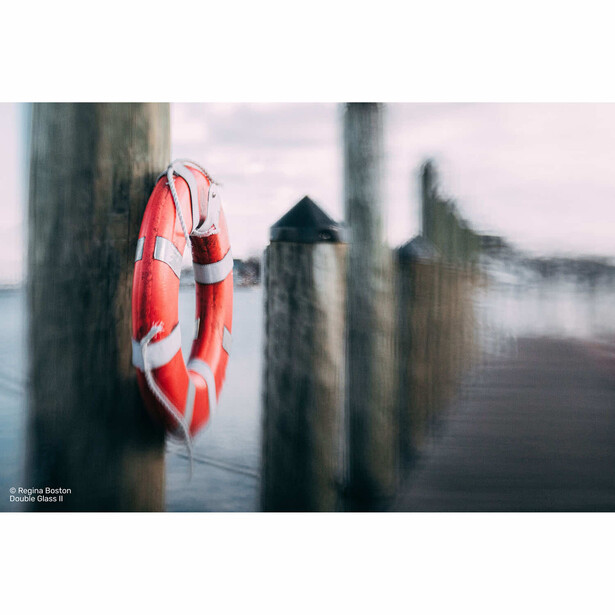Red and white life preserver ring mounted on weathered wooden post with blurred background.