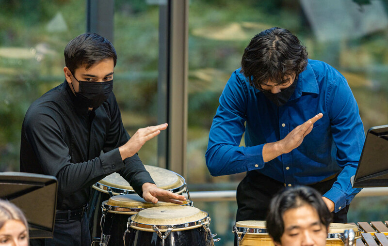 Two musicians demonstrating hand positions on timpani drums during an instructional session.