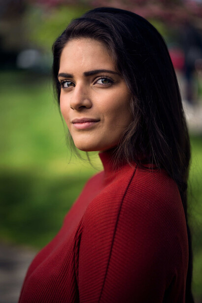 Woman in red cardigan looking over shoulder at camera with blurred green background.