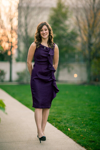 Woman in purple ruched dress walking on tree-lined path during golden hour.