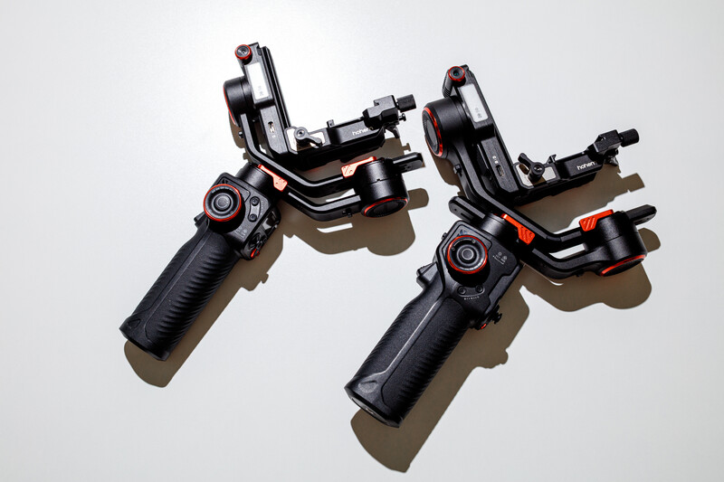 Two gimbal stabilizers with black handles and red accents displayed on white background.