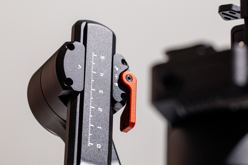Close-up of a camera flash meter with gray measurement scale and red adjustment lever against blurred background.