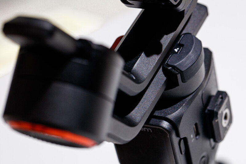 Close-up of a three-axis gimbal stabilizer mounted on a smartphone, with selective focus on the mechanical arms and controls.