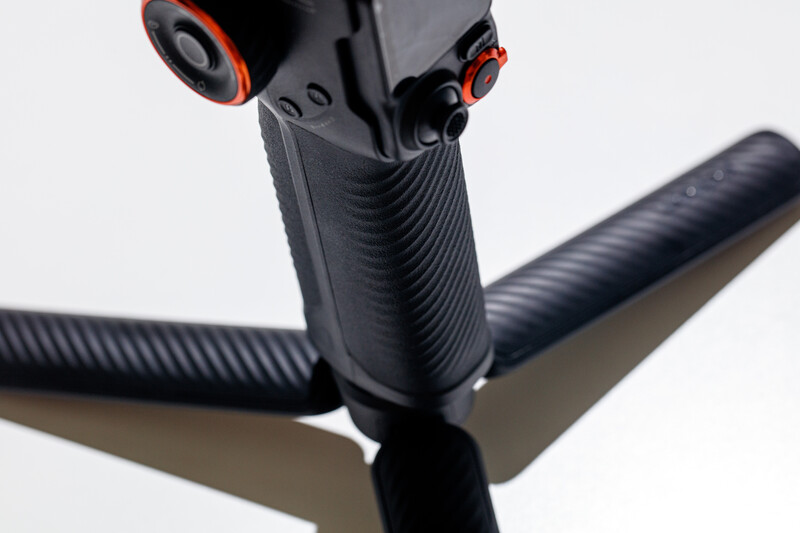 Close-up of a three-axis gimbal stabilizer with black rubberized handles and red accent details.