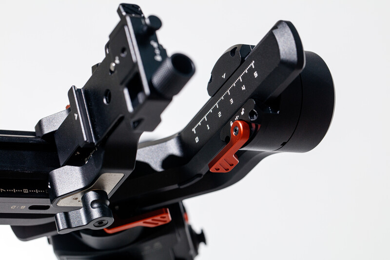 Close-up of a camera follow focus system with red accent lever and numbered focus ring against white background.