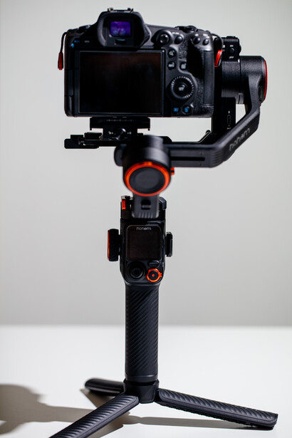 Three-axis gimbal stabilizer with mirrorless camera mounted on top and tripod base below.