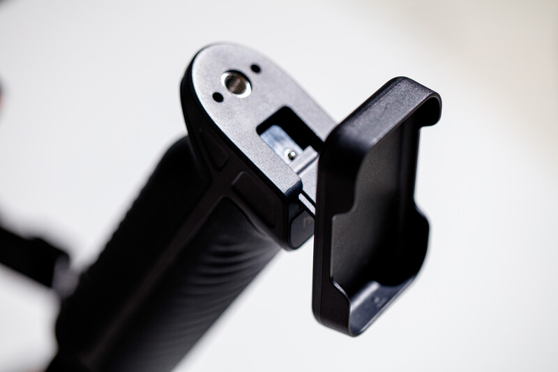 Close-up of a smartphone holder mounted on a black grip handle with a white adjustment mechanism visible.