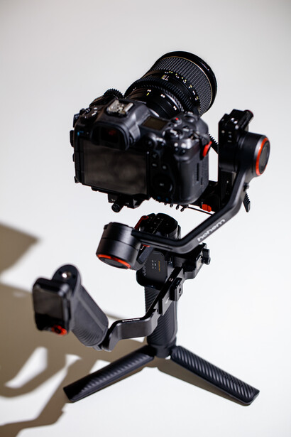 Professional camera gimbal stabilizer mounted on tripod with DSLR and telephoto lens attached.