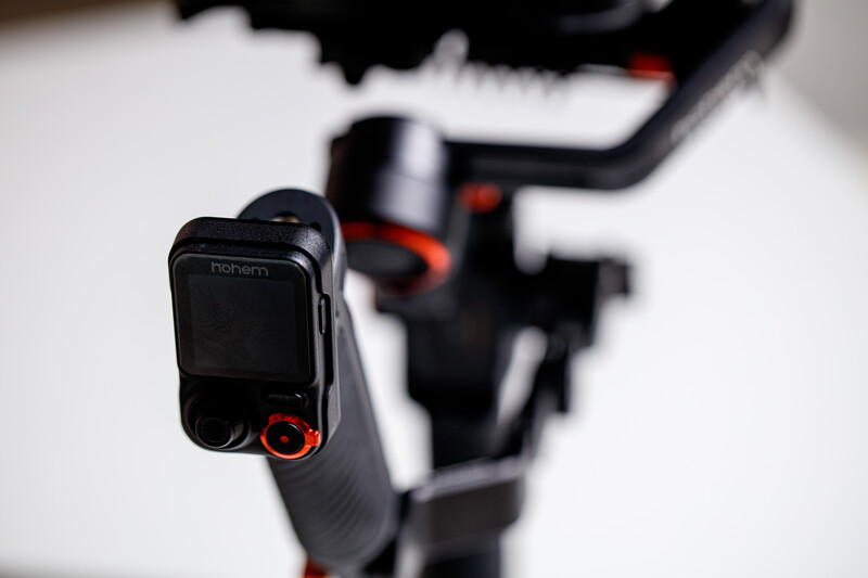 Close-up of a camera gimbal's control handle with red accents and interface buttons in sharp focus.