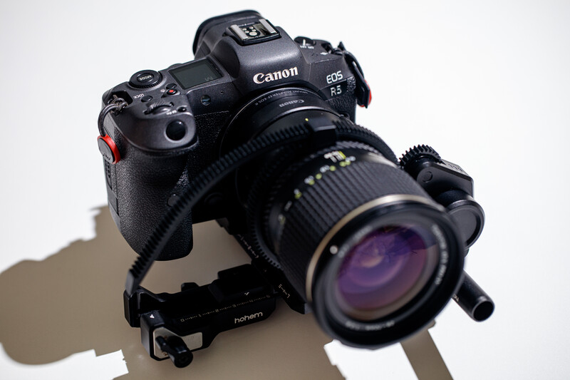 Canon EOS R5 mirrorless camera with telephoto lens mounted, positioned on a light surface against a white background.
