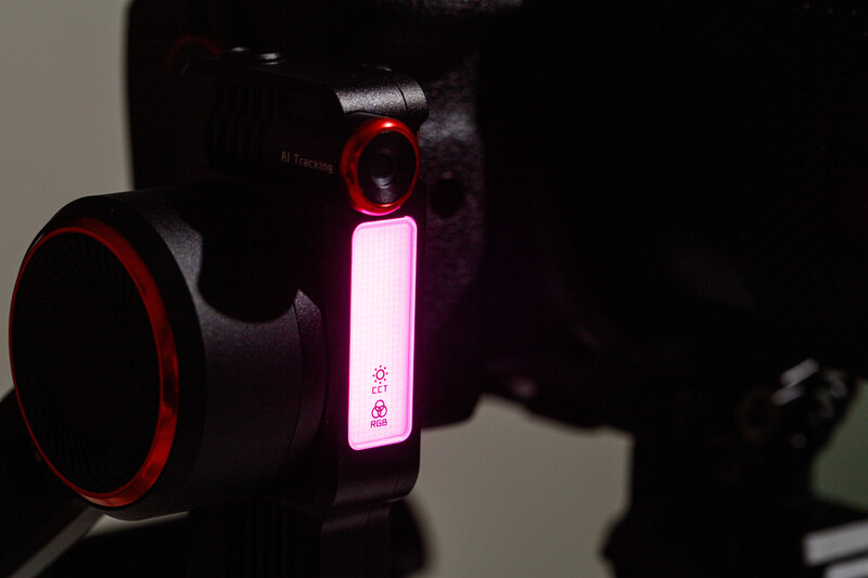 Pink neon light modifier attached to camera with red accents in dark studio setting.