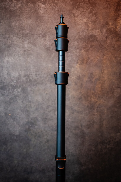 Vertical studio product shot of a black telescope or lens assembly against a textured brown backdrop.