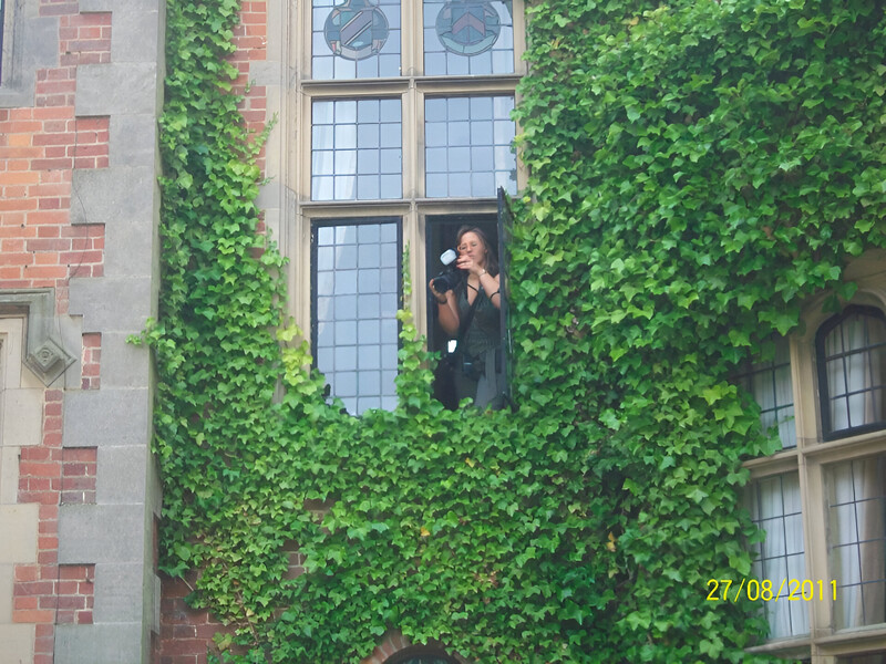 Person in dark clothing standing at a window framed by ivy-covered walls and large paned windows.