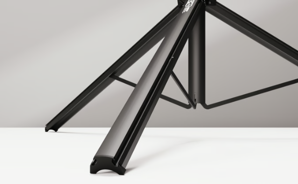 Close-up of a tripod's leg assembly and base with black metal construction against a neutral background.