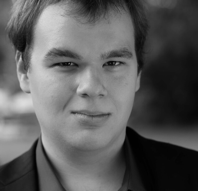 Black and white headshot portrait of a man with short dark hair, looking directly at camera with a slight smile.