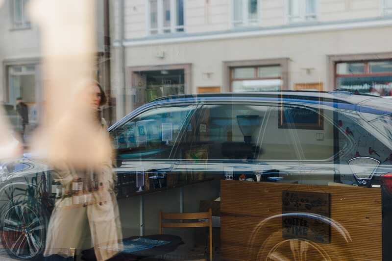 Double exposure of parked blue SUV and storefront interior with wooden counter and bicycle wheel.