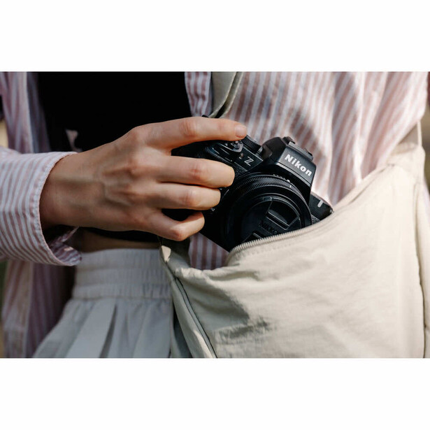Photographer holding a black DSLR camera while wearing a striped shirt and light-colored vest.