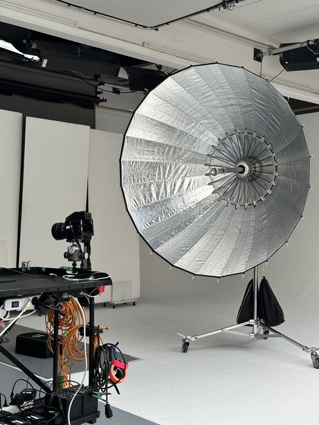 Studio lighting setup with large parabolic reflector mounted on a stand next to camera rig.
